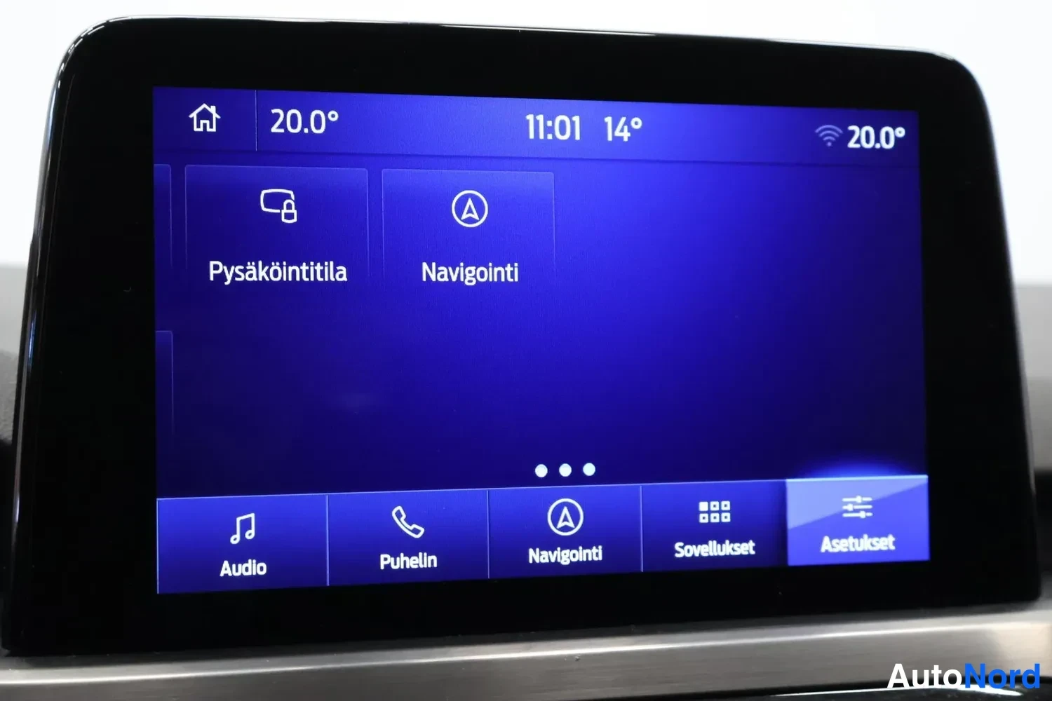 Muu: Auton keskusnäyttö, jossa näkyvät Pysäköintitila ja Navigointi sekä alavalikot Audio, Puhelin, Navigointi, Sovellukset ja Asetukset.