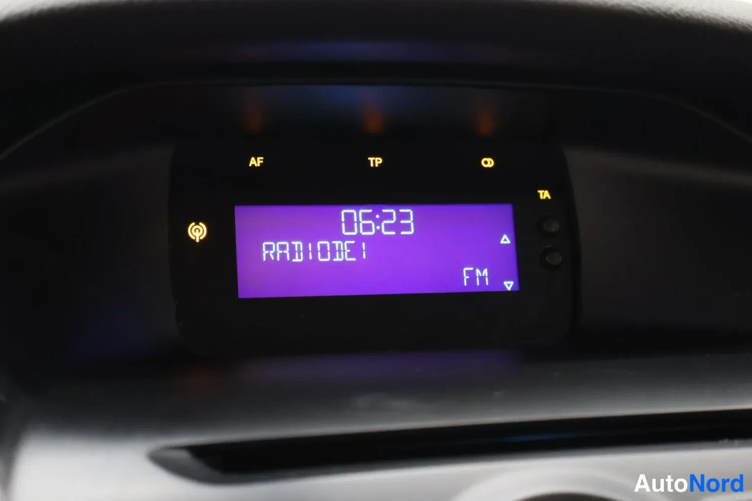 Yksityiskohta: Radiopaneelin näyttö, jossa kello 06:23, kanava RADIODE1 ja FM-merkintä.
