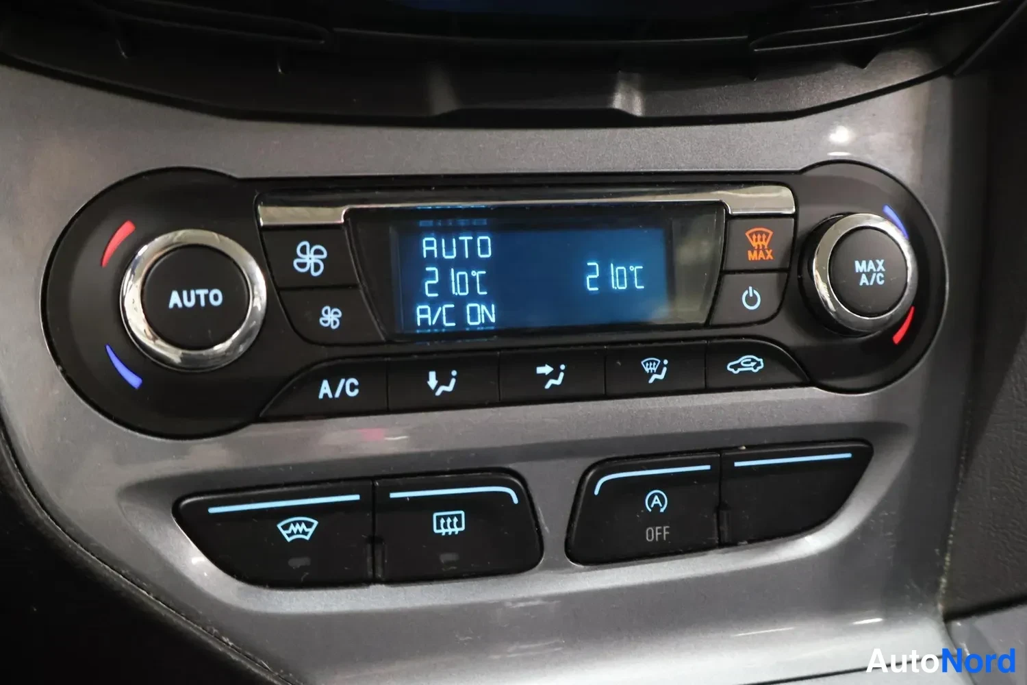 Yksityiskohta: Kaksivyöhykkeinen automaattinen ilmastointipaneeli, jossa AUTO-, A/C- ja MAX A/C -painikkeet ja lämpötilat 21 °C.