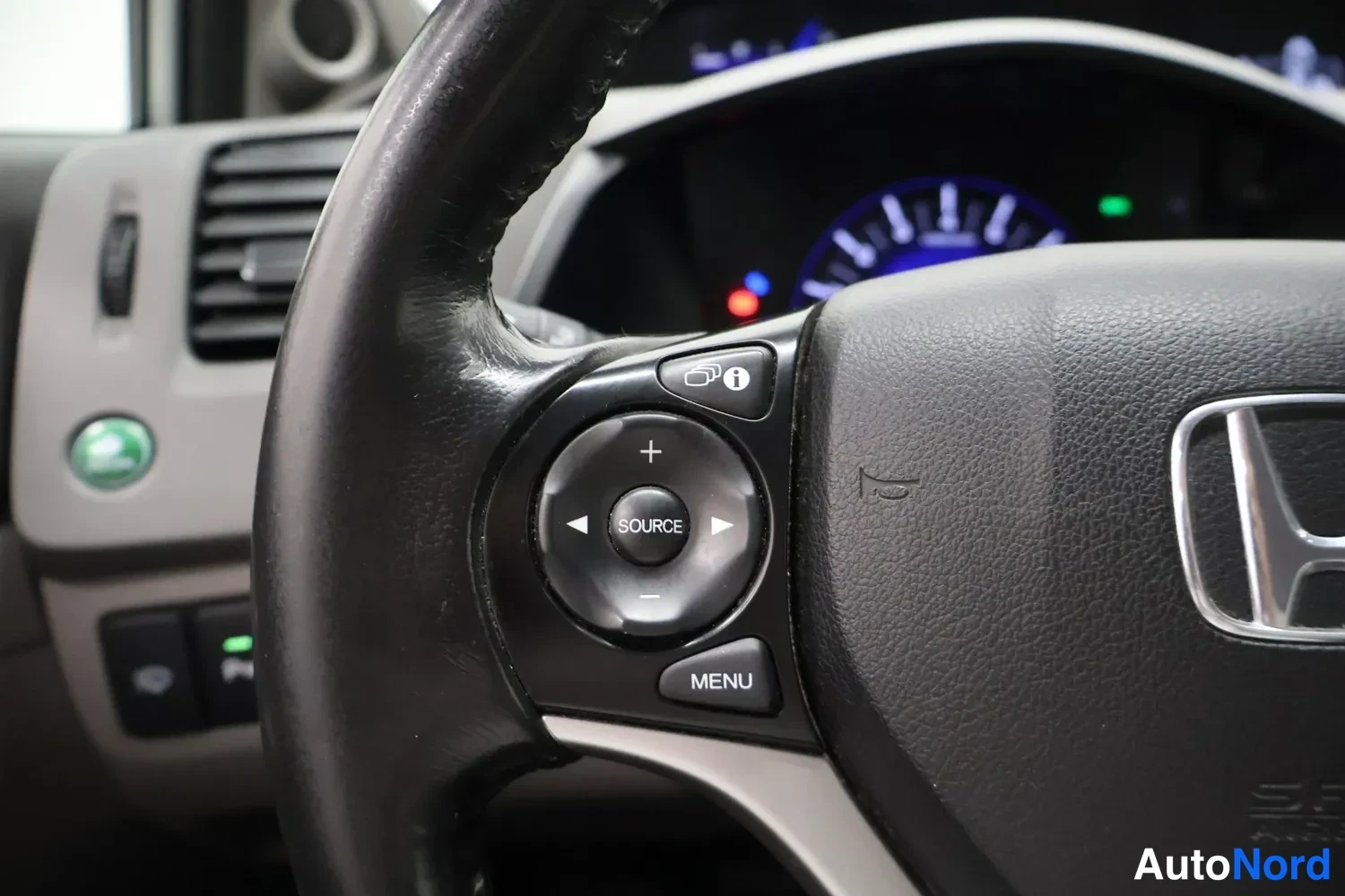 Yksityiskohta: Ohjauspyörän vasen puhelin: SOURCE-nuolinäppäimet, MENU-painike ja info-näppäin, Honda-logo näkyvissä.
