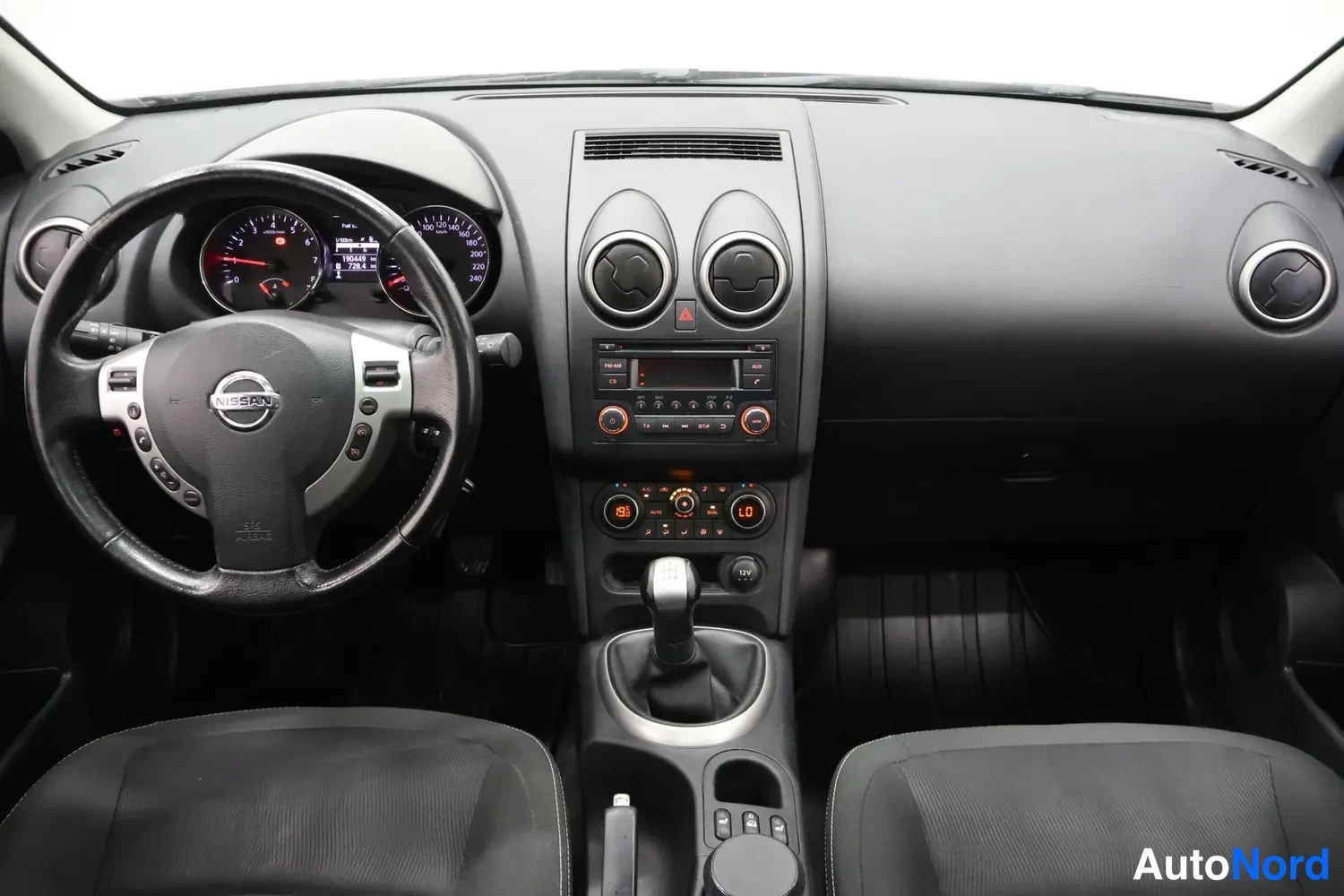 Muu: Ohjaamosta ylhäältä kuvattu näkymä: Nissan-ohjauspyörä, mittaristo, keskikonsolin radio ja ilmastointilaitteet sekä manuaalivaihteiston vaihteenkeila.