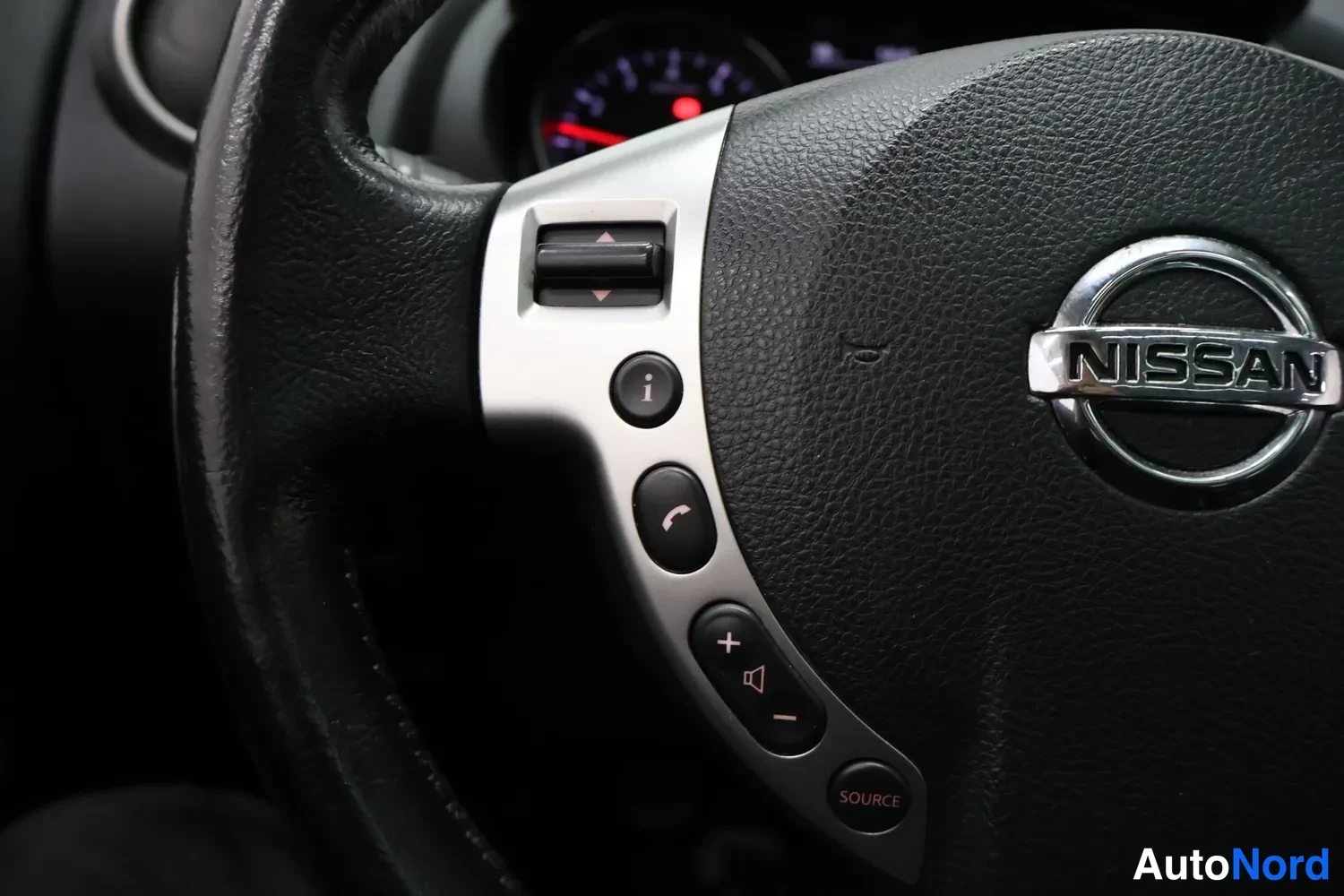 Muu: Nissan-ohjauspyörän lähikuva, jossa näkyvät merkkivalot ja äänenvoimakkuudensäätöpainikkeet.