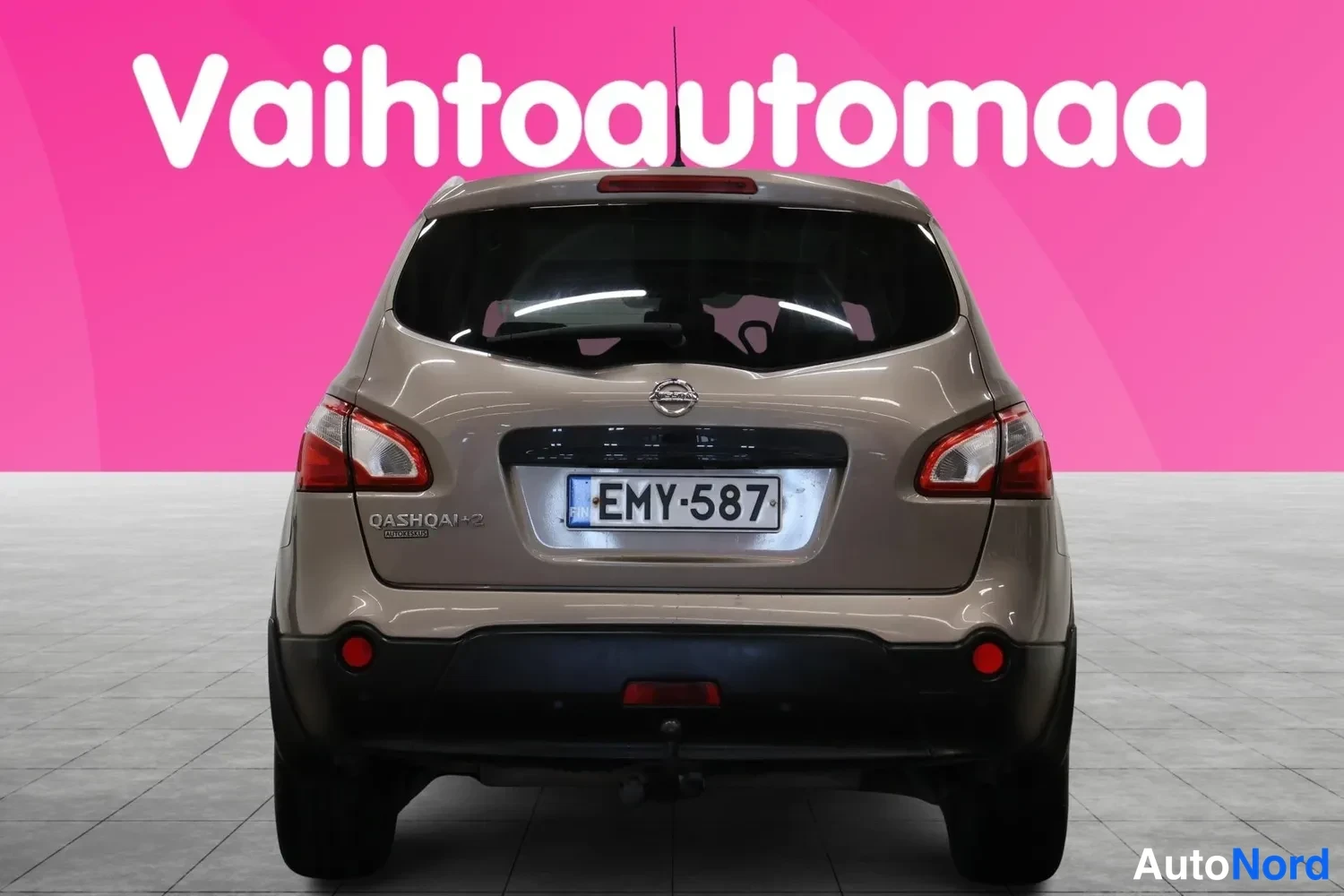 Takaa: Auton takaosa suoraan takaa: ruskeanbeige Nissan, rekisterikilpi, takavalot ja takapuskuri näkyvät.