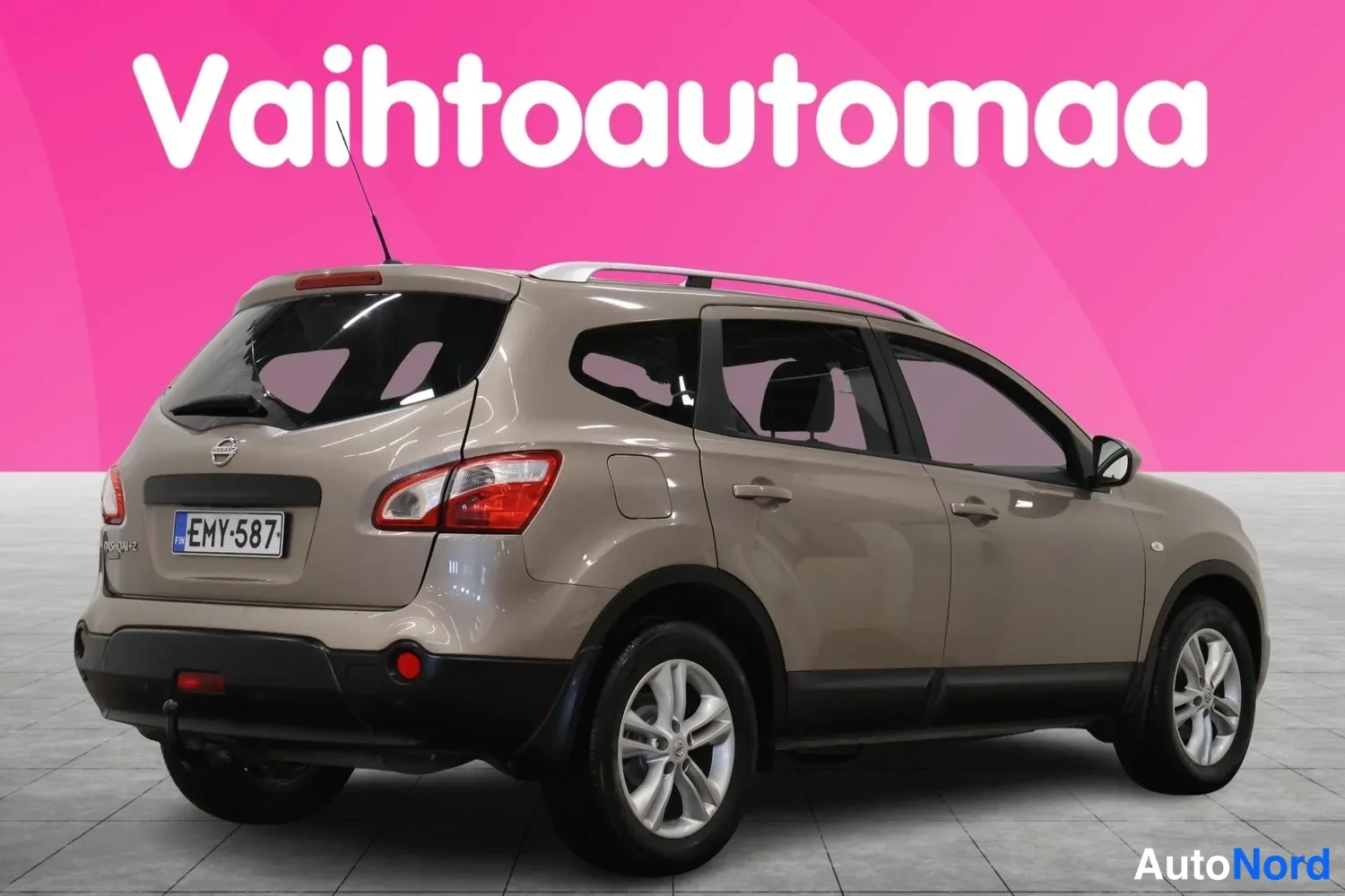 Takaviisto: Auton takakulma toisesta suunnasta: ruskeanbeige Nissan, rekisterikilpi, kattokaide ja perävaunun kytkin näkyvät.