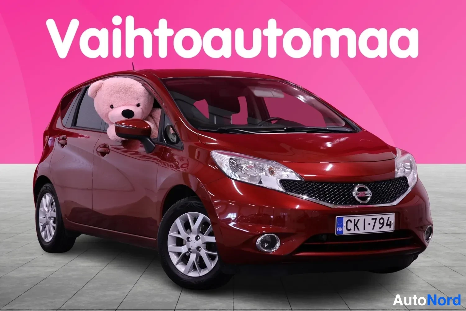 Etuviisto, nokka oikealle: Tummanpunaisen Nissan Note -henkilöauton etusivu kulmasta, keulakilpi näkyvissä.