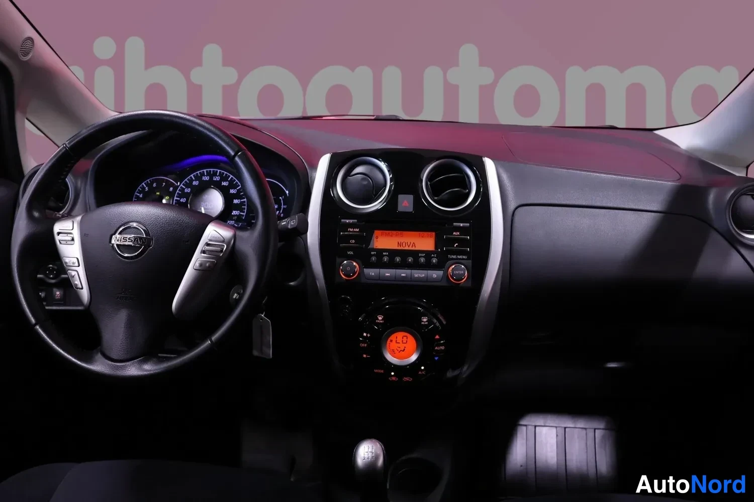 Muu: Kojelauta suoraan edestä: Nissan-ohjauspyörä, pyöreät tuuletusaukot, radio näytöllä 'NOVA' ja ilmastointipaneeli näytöllä 'LO 34'.