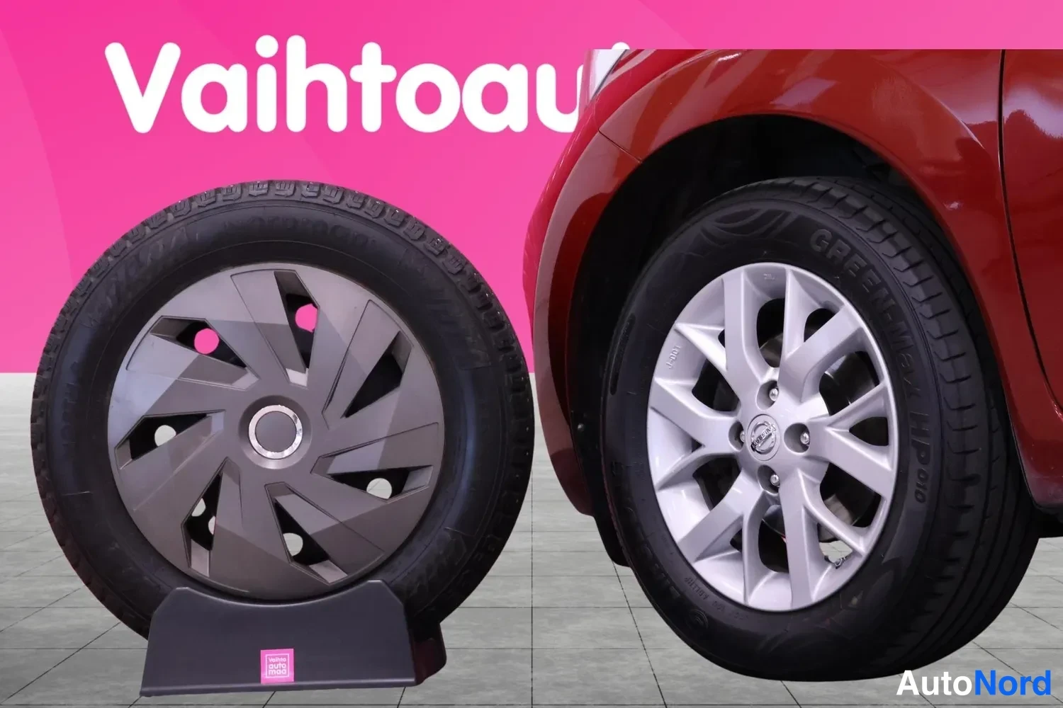 Yksityiskohta: Vaihtoautot-tunnusta ja kaksi pyörää: vasemmalla pölykapsellinen varapyörä jalustalla, oikealla auton hopeavanne ja GreenMax HP010 -renkaassa punaisen korirungo