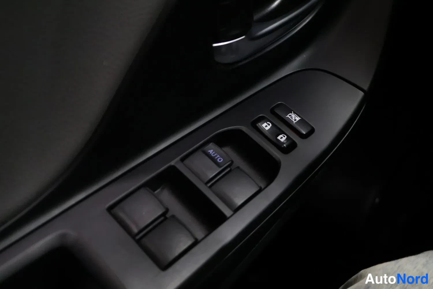 Yksityiskohta: Auton oven sisäpaneeli, jossa sähköikkunoiden kytkimet, AUTO-merkitty painike, keskilukituksen painikkeet ja peilien taittopainike.