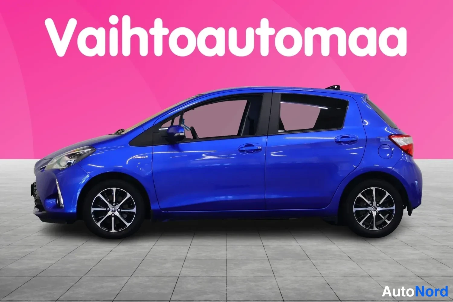 Etuviisto, nokka vasemmalle: Sininen Toyota Yaris -henkilöauto sivulta, keula kuvan vasemmassa reunassa.