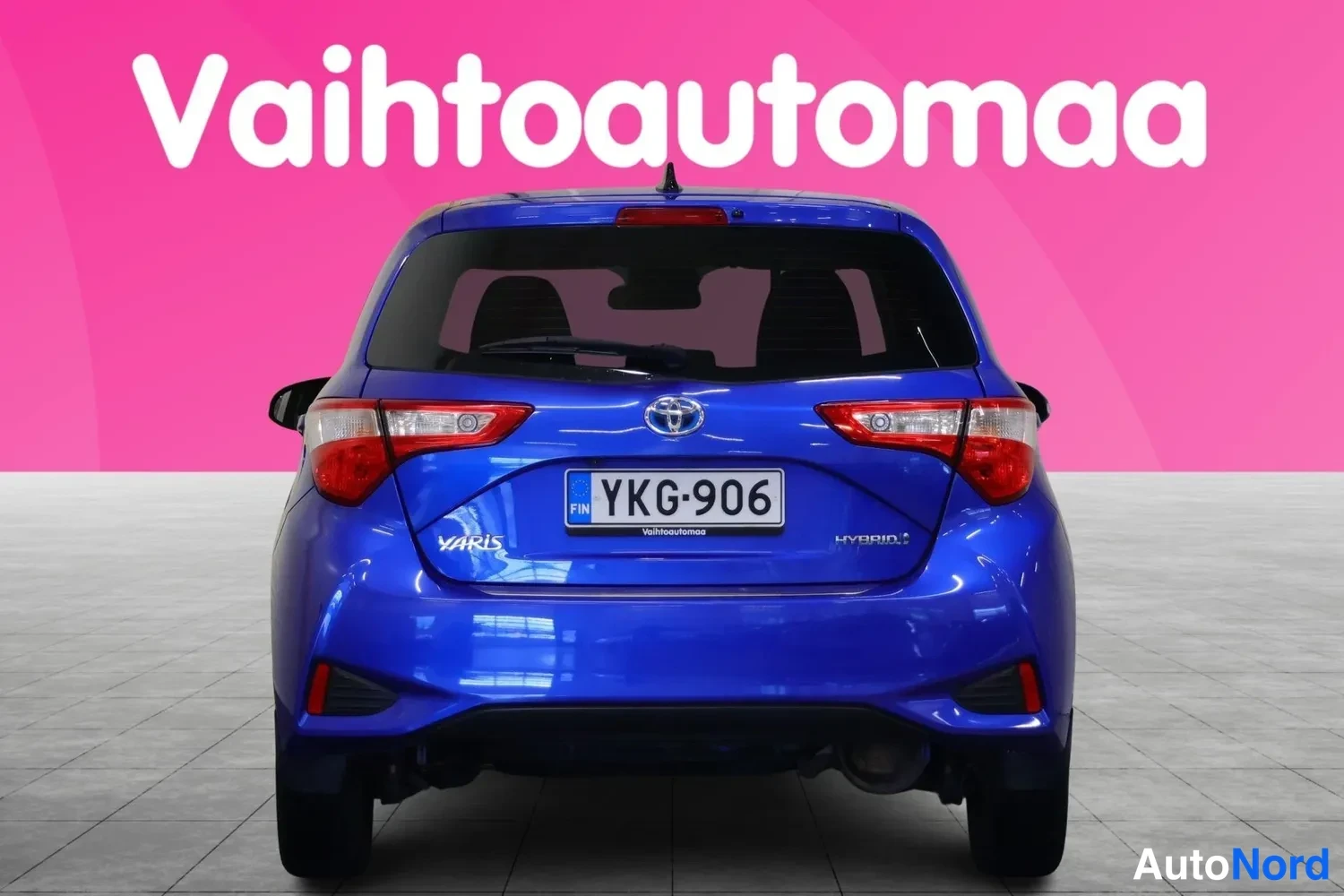 Takaa: Sininen Toyota Yaris -henkilöauto suoraan takaa, rekisterikilpi, takaluukussa YARIS- ja HYBRID-tekstit.