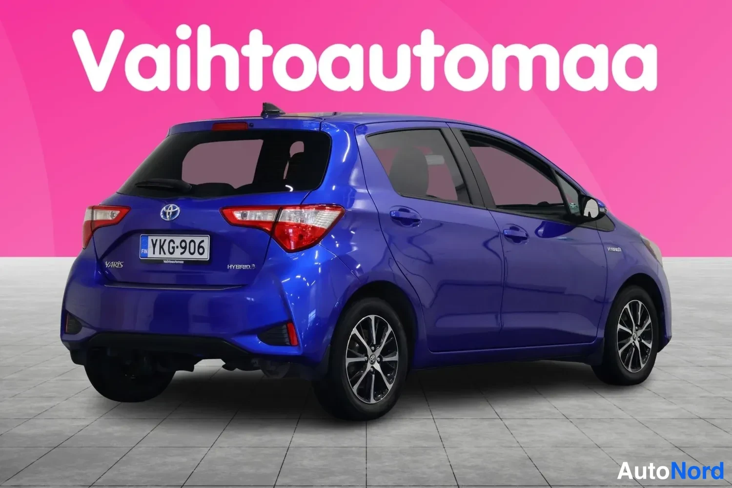 Takaviisto: Sininen Toyota Yaris Hybrid -viistoperä kuvattu takaa viistosti; rekisterikilpi ja HYBRID-merkintä takaluukussa näkyvät.