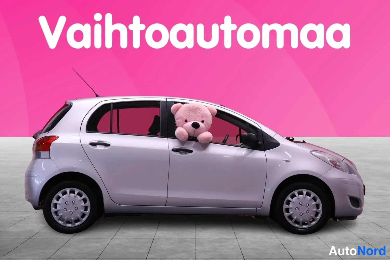 Sivulta: Hopeanharmaa Toyota Yaris sivusta, nallekuva ikkunassa.