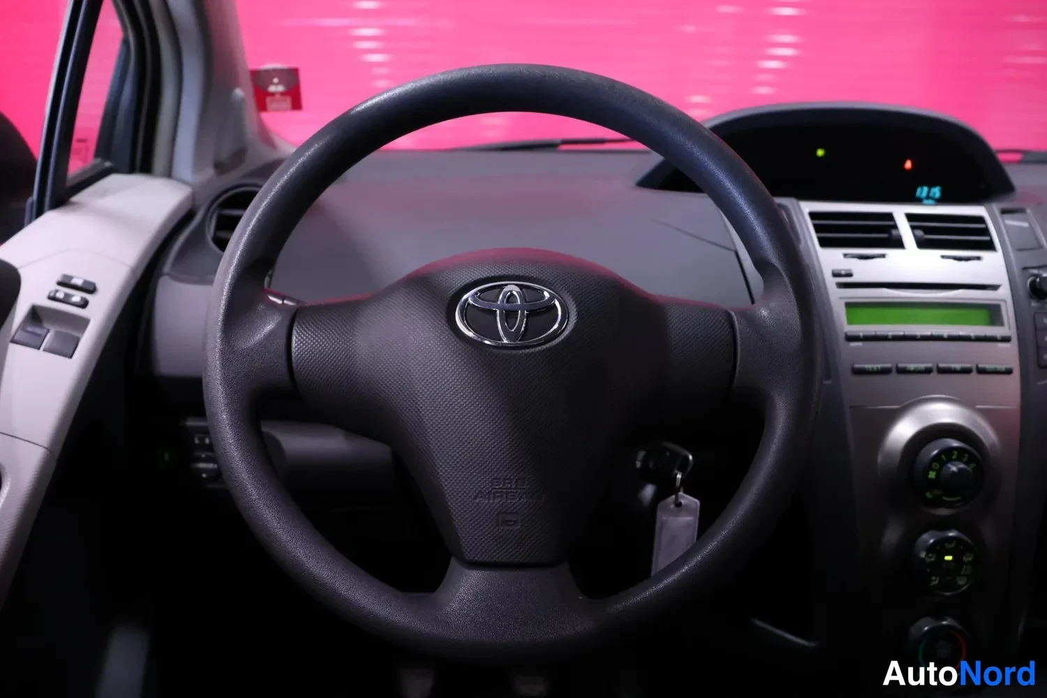 Muu: Ohjauspyörä lähikuvassa, Toyotan merkki keskellä, kojelauta ja radionäyttö taustalla.
