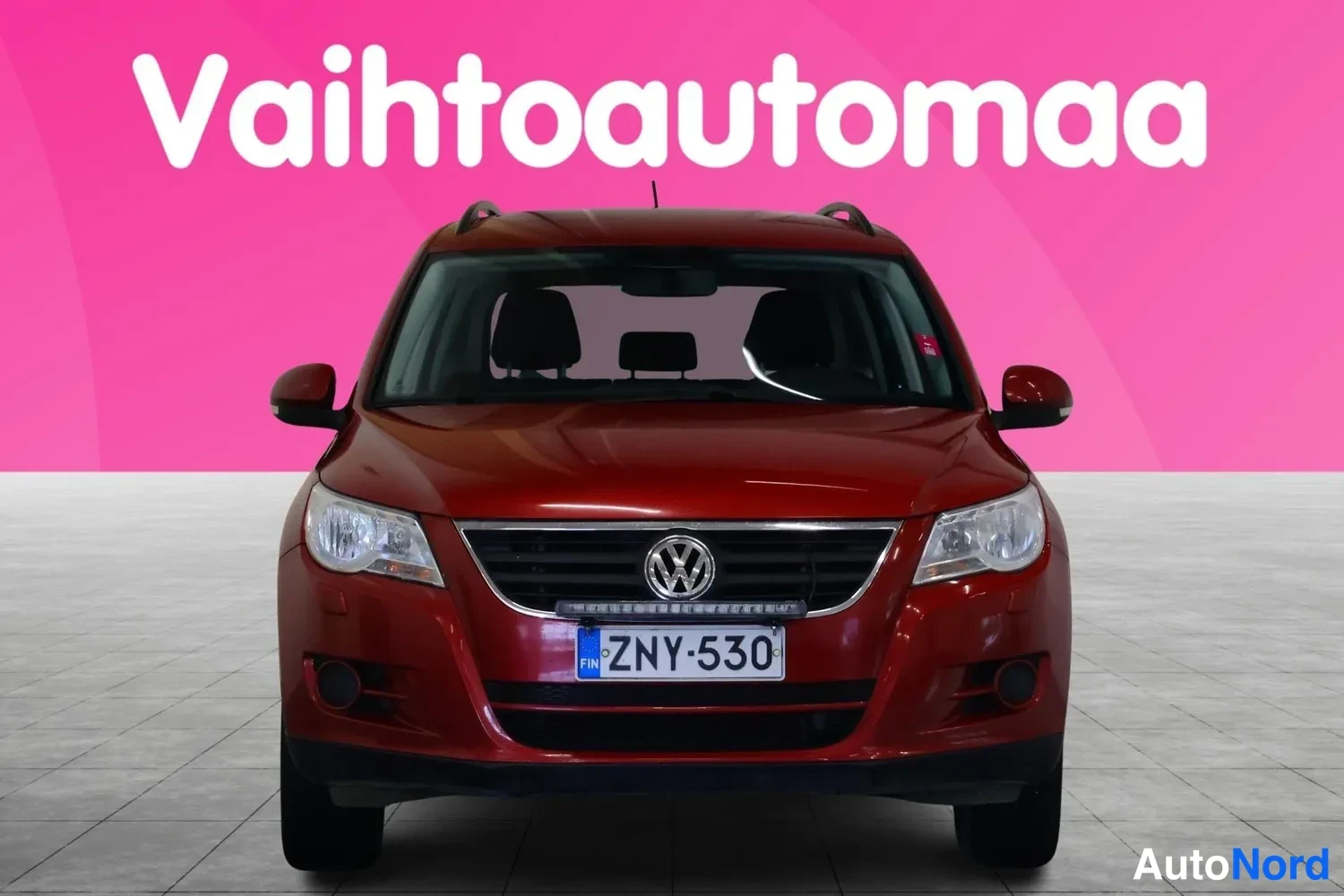 Edestä: Punainen Volkswagen Tiguan suoraan edestä päin, rekisteritunnus.