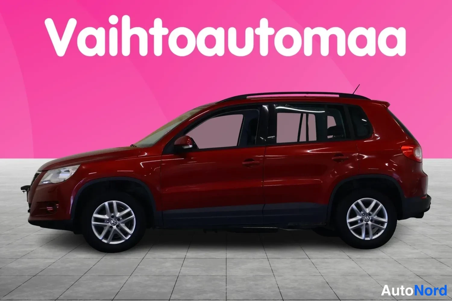 Sivulta: Punaisenruskea Volkswagen Tiguan sivusta vasemmalta, kattokaiteet näkyvissä.