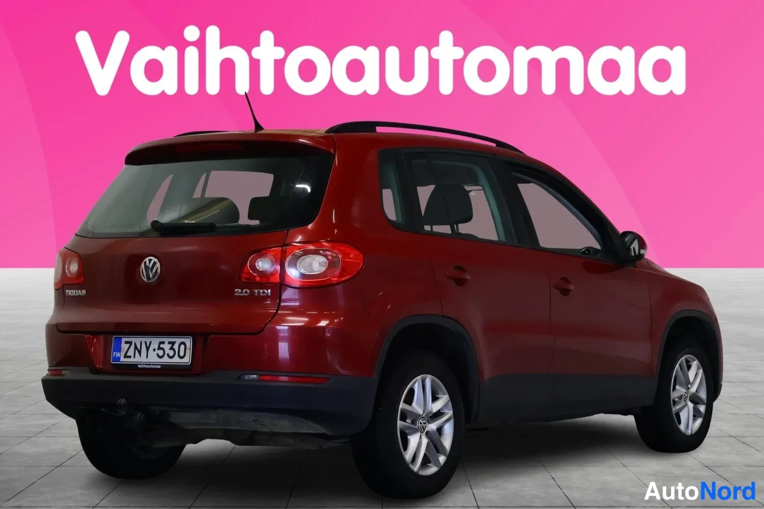 Takaviisto: Punainen Volkswagen Tiguan takaa kolmivartinäkymässä, takavalot, VW-merkki ja 2.0 TDI -merkintä näkyvissä, rekisterikilpi, katolla kattokaiteet ja takaosan veto