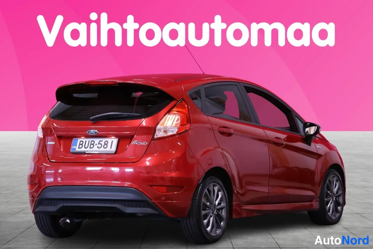 Takaviisto: Punainen Ford Fiesta takaviistöstä vasemmalta, rekisterikilpi.