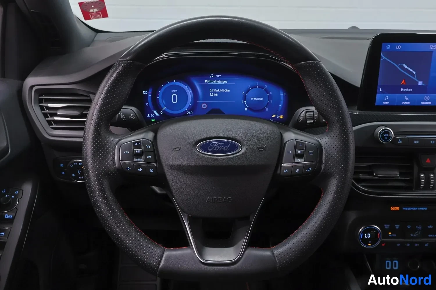 Muu: Lähikuva ohjauspyörästä ja digitaalisesta mittaristosta, keskellä Ford-tunnuksella varustettu pörrönen ja AIRBAG-teksti.