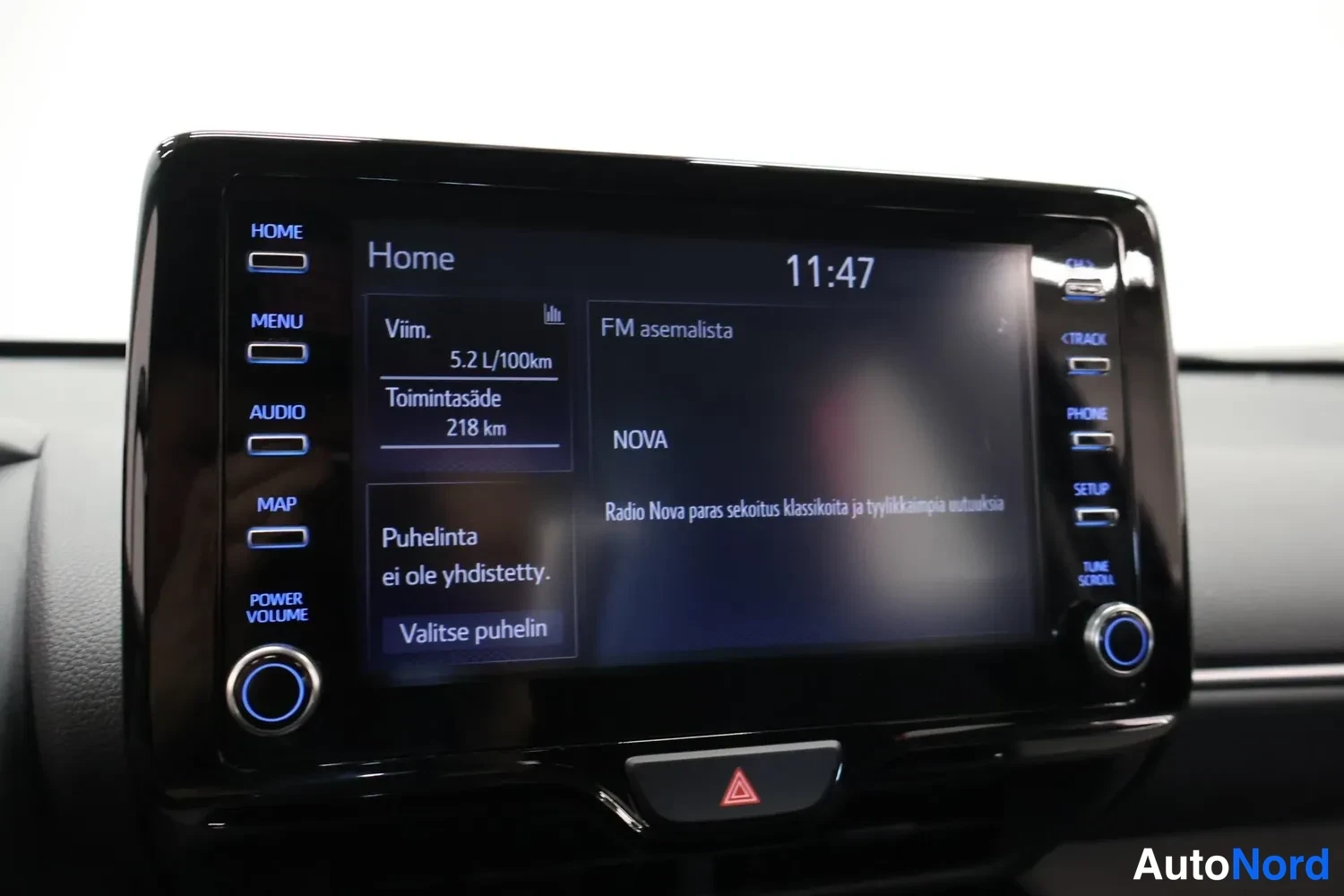 Yksityiskohta: Auton kosketusnäytöllä näkyy Home-valikko, kello 11:47, keskimääräinen kulutus 5,2 l/100 km, toimintasäde 218 km ja FM-asemalista Radio Nova.