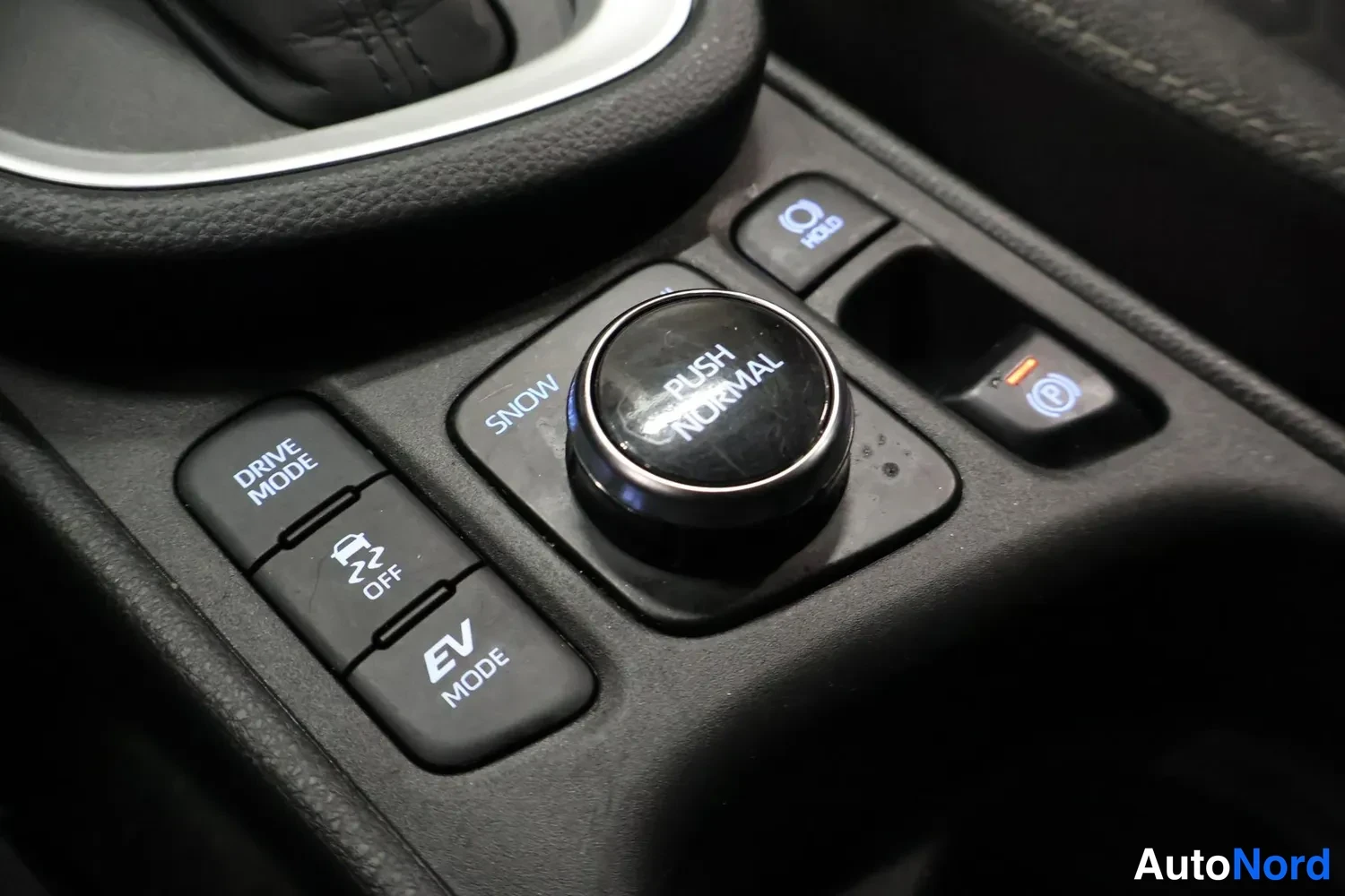 Yksityiskohta: Keskikonsolin ajotilakatkaisimet: PUSH NORMAL -kytkin, SNOW, DRIVE MODE, OFF ja EV MODE -painikkeet sekä HOLD ja parkkir刚性-merkinnät.