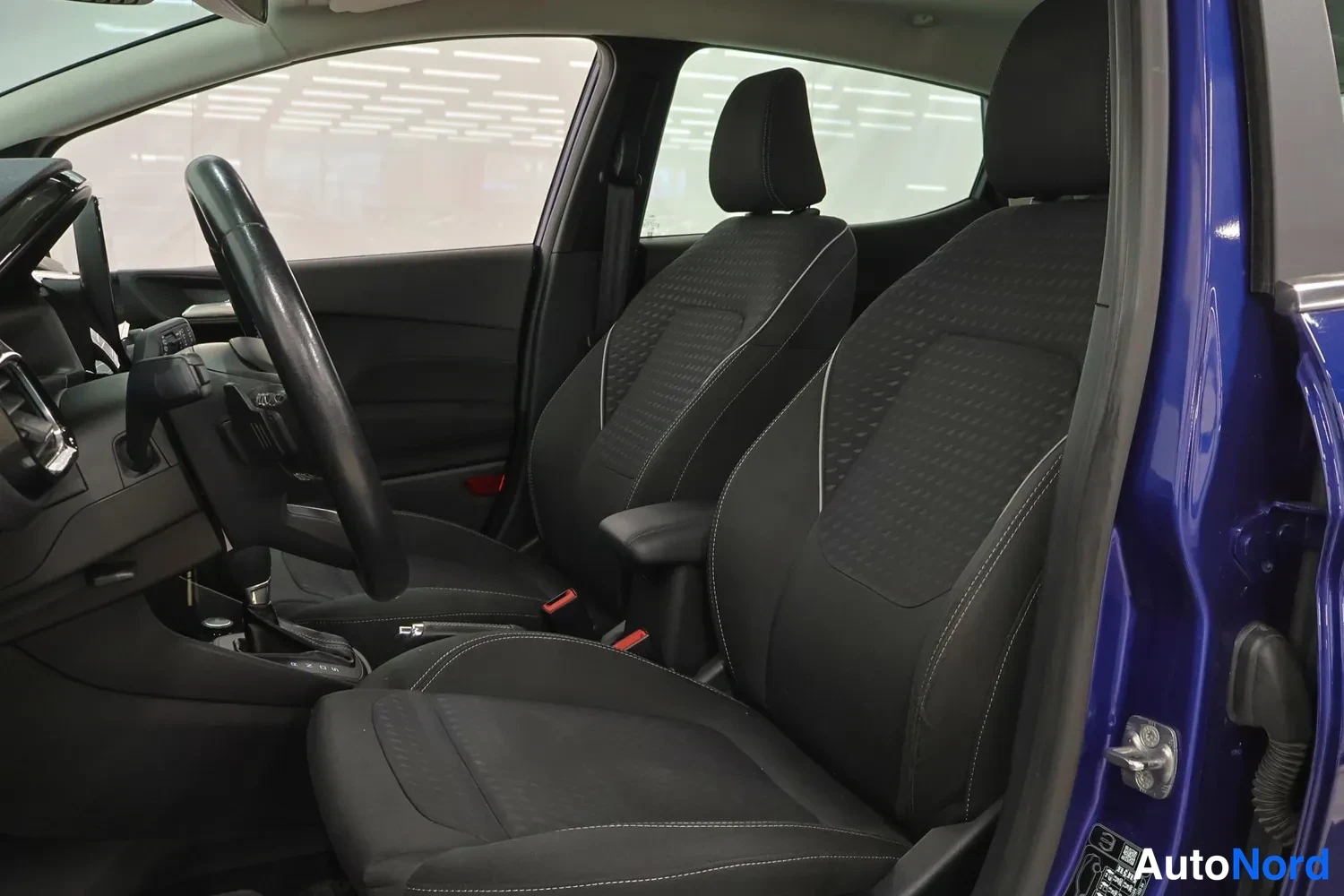 Muu: Ford Fiestan etusomapenkki mustaa kuviollista kangasta, ohjauspyörä ja etuoviaukon sininen runko.