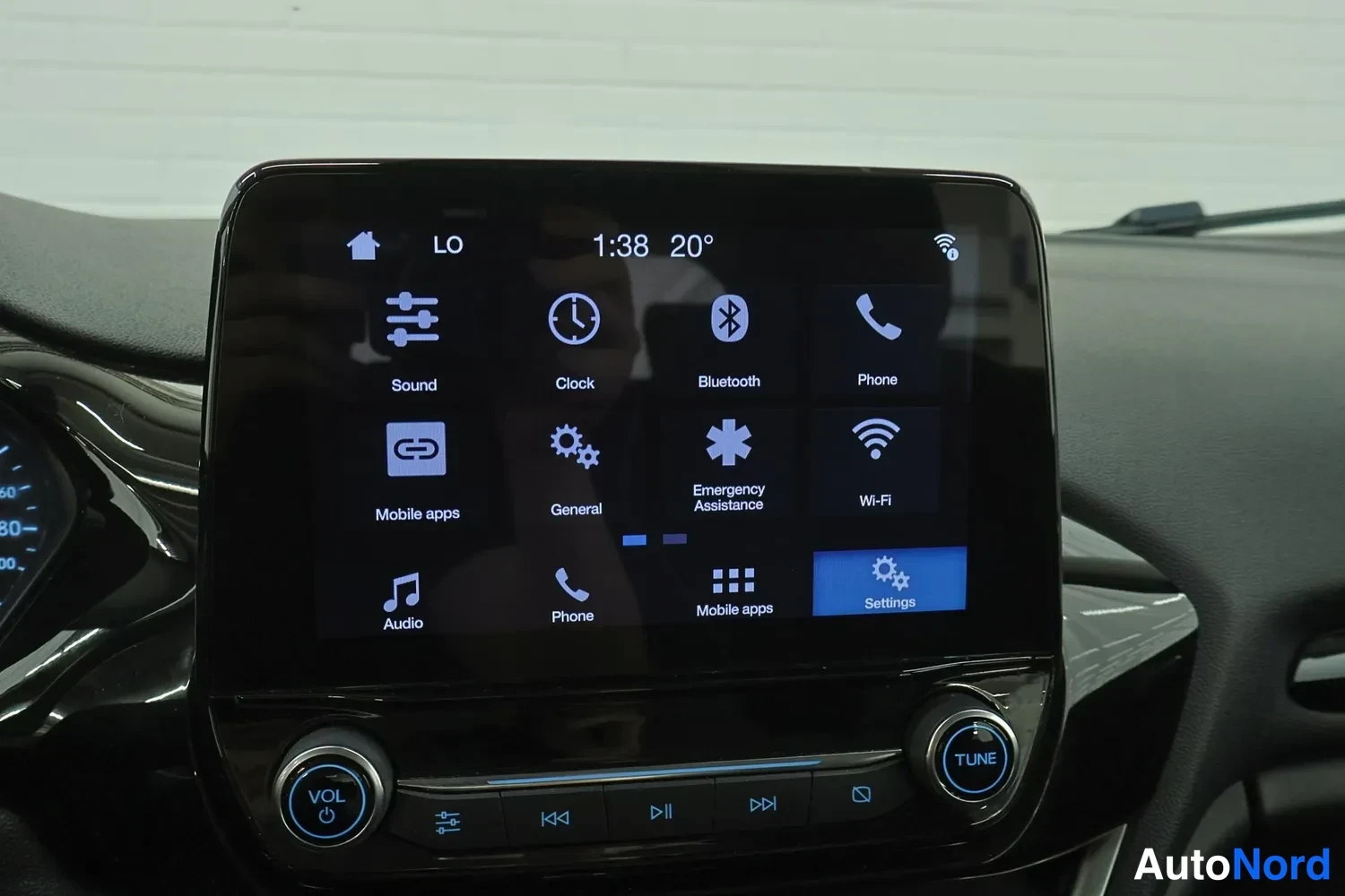 Yksityiskohta: Ford-auton kosketusnäytön valikko näkyvissä valokuvalla, 20° lämpötila näytöllä ja mediapaneelin VOL- ja TUNE-keittimet.