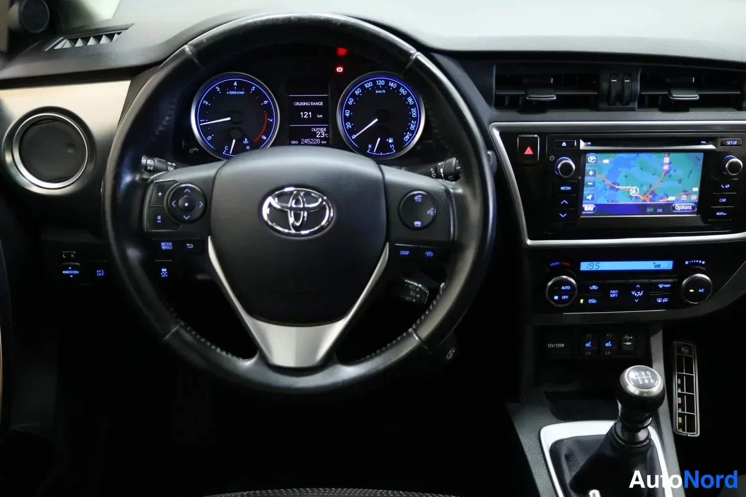 Yksityiskohta: Toyota Aurisin ohjaamo: ratti, kellotaulusto (matkamittari 245228 km), manuaalivaihteerin nuppi, kosketusnäytöllinen navigointilaite ja automaattinen ilmastoint