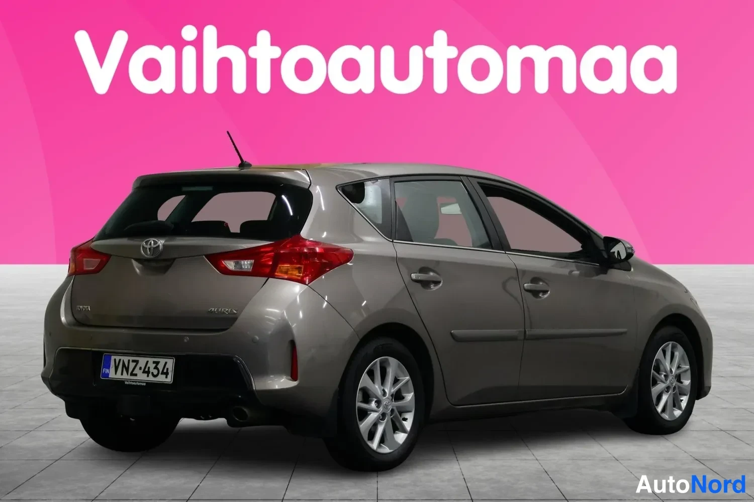 Takaviisto: Toyota Auris -farmarin/hahtikassin takakulma vasemmalta, tummanharmaa korit väri, rekisterikilpi, valkoinen tausta pinkillä mainospaneelilla.