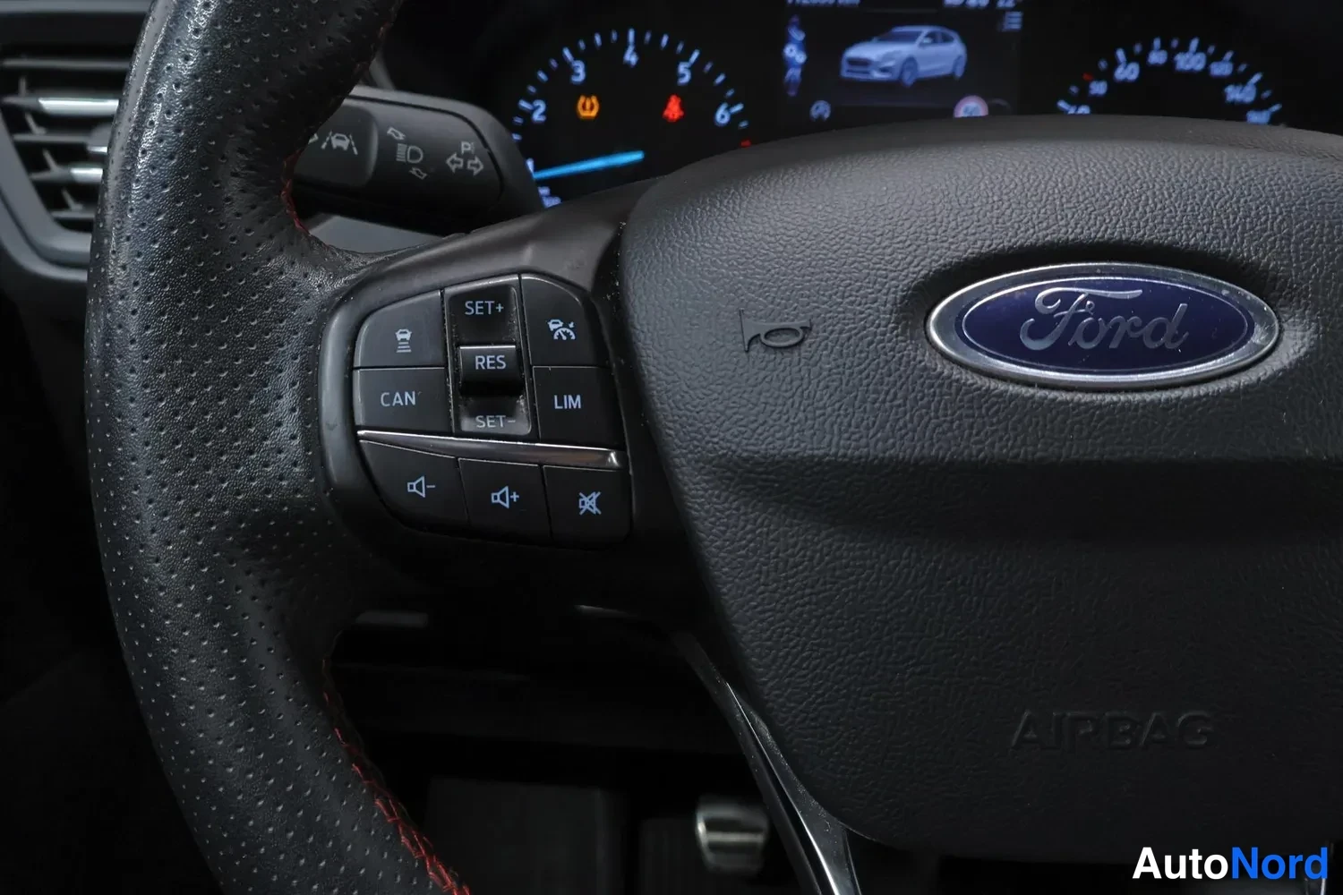 Muu: Lähikuva Ford-ohjauspyörästä ja sen vasemmasta palkista, AIRBAG-teksti