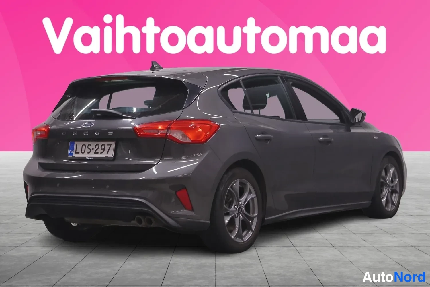 Takaviisto: Tummaharmaa Ford Focus -henkilöauto takaviistosta, rekisterikilpi, vaaleansinistä taustaa vasten.