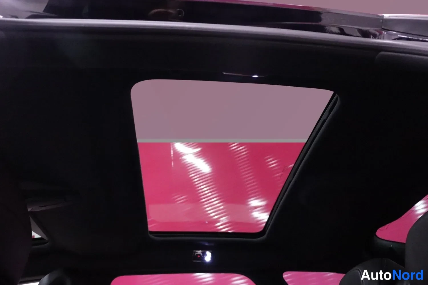Muu: Panoraamakattoluukku autosta sisältä nähtynä, tumma katto ja pinkki tausta luukun läpi.