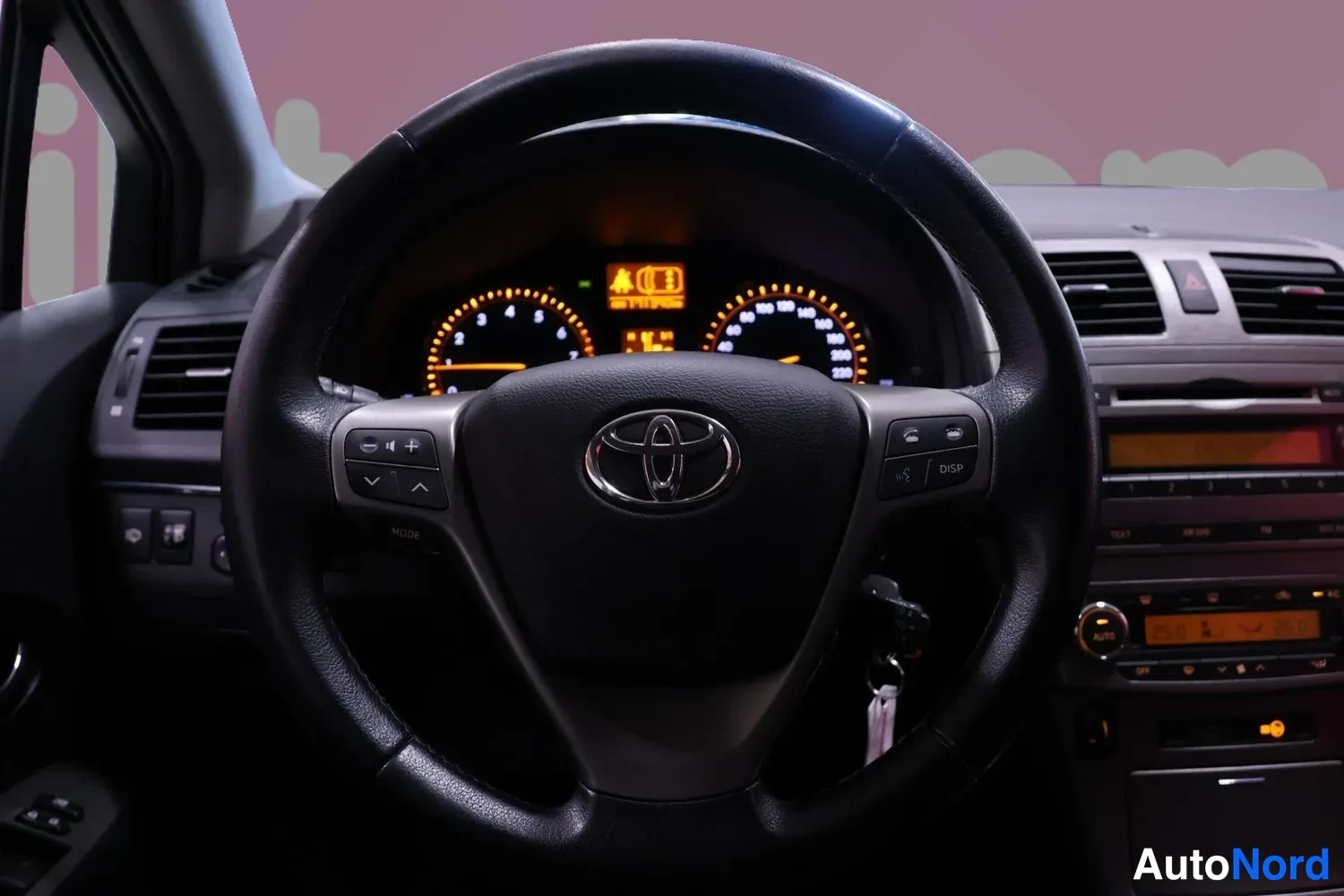 Muu: Ohjaamon sisäkuva: Toyota-merkkinen ohjauspyörä, valaistu mittaristo nopeus- ja kierrosmittareineen sekä kojelauta radion ja ilmastoinnin säätimineen; avain on