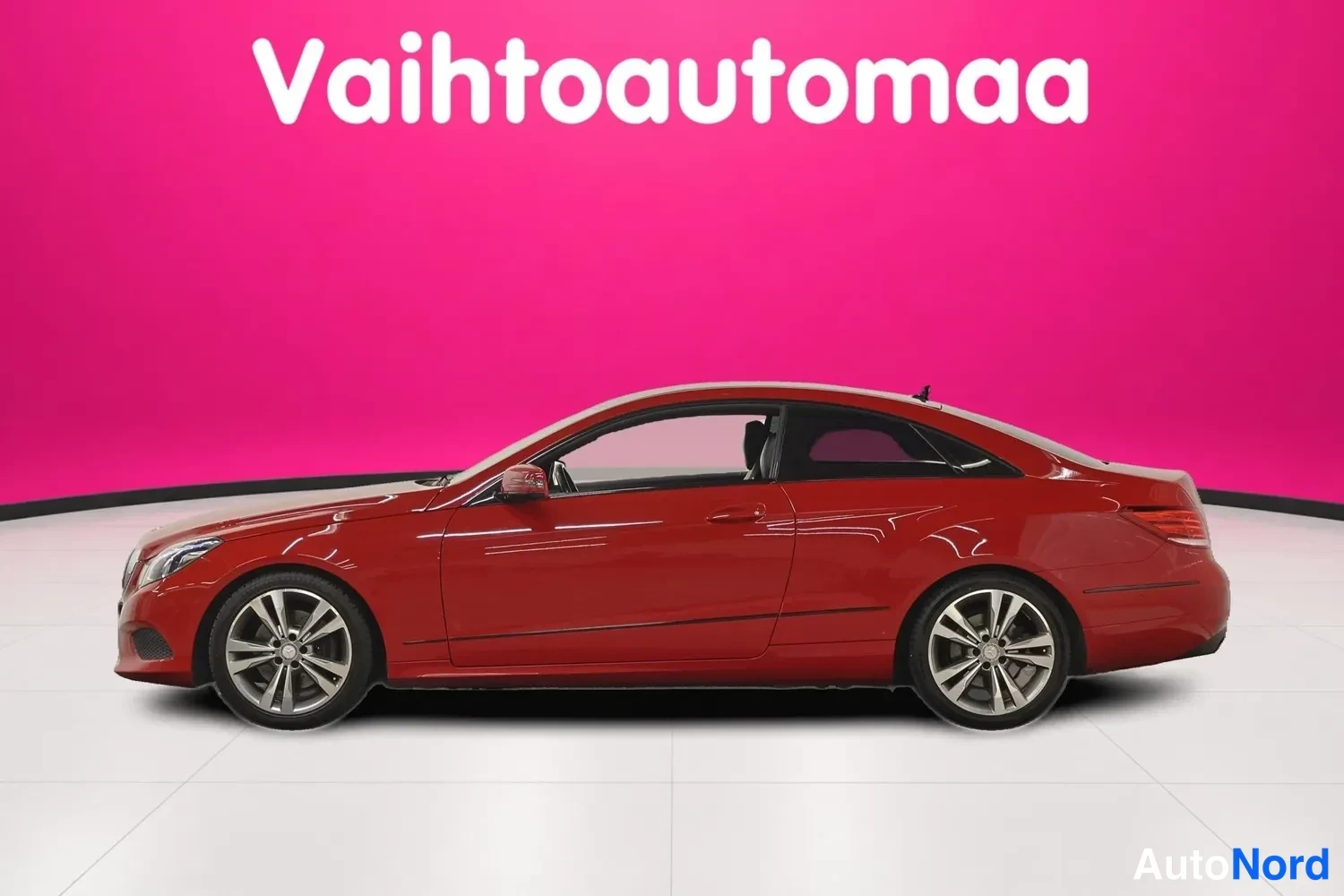 Sivulta: Punainen Mercedes-Benz E 200 -coupe sivusta oikealta valkoisessa studiossa pinkin taustan edessä.