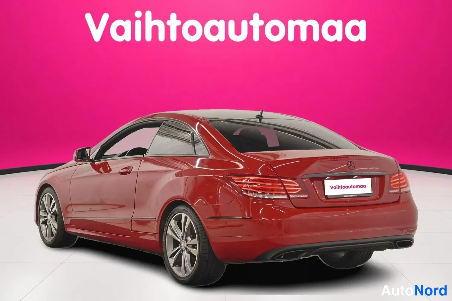 Takaviisto: Punainen Mercedes-Benz E 200 -coupe kolmesta neljäsosasta takaa vasemmalta valkoisessa studiossa pinkin taustan edessä.