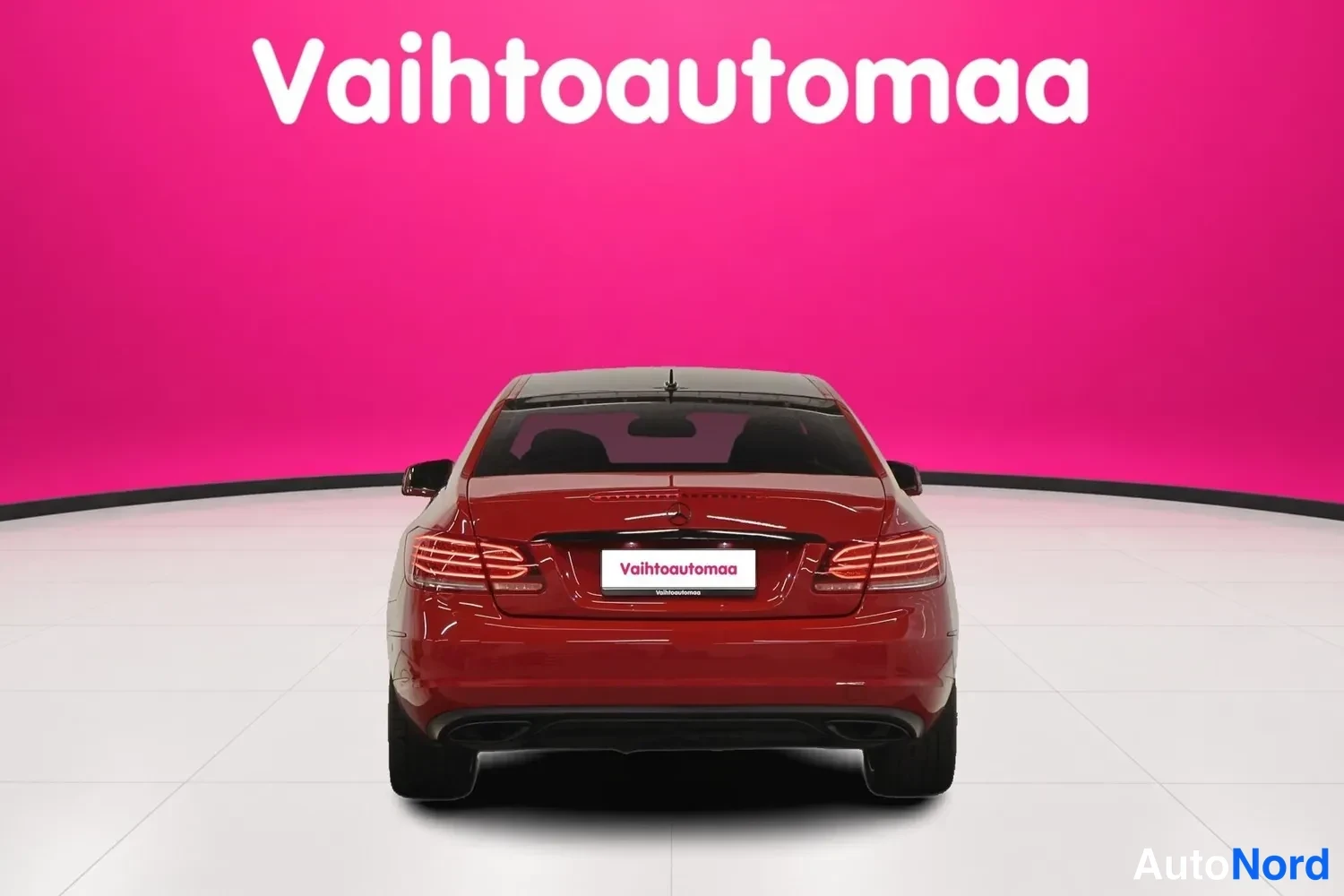 Takaa: Punainen Mercedes-Benz E 200 -coupe suoraan takaa valkoisessa studiossa pinkin taustan edessä.