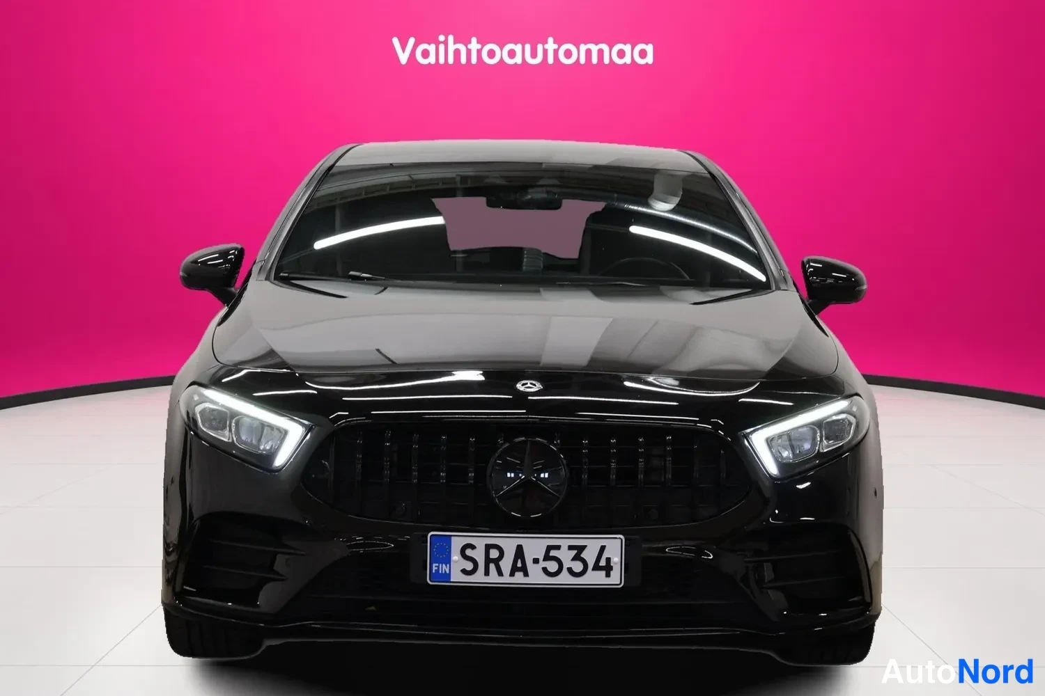 Edestä: Mustan Mercedes-Benz A-luokan auton suora etunäkymä: maski, Mercedes-tähti, ohut-LED-ajovalot ja rekisteri.