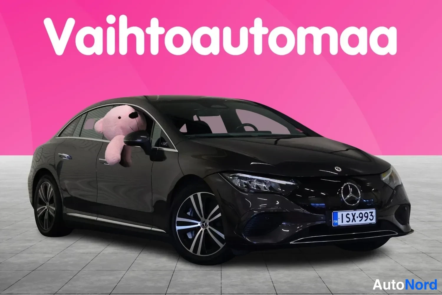 Etuviisto, nokka oikealle: Mercedes-Benz EQE -sedanin etukulmakuva tummanruskeahkon metallivärinä kori, etusäleikkö ja rekisterikilpi näkyvät; kilpi FIN-tunnuksella.