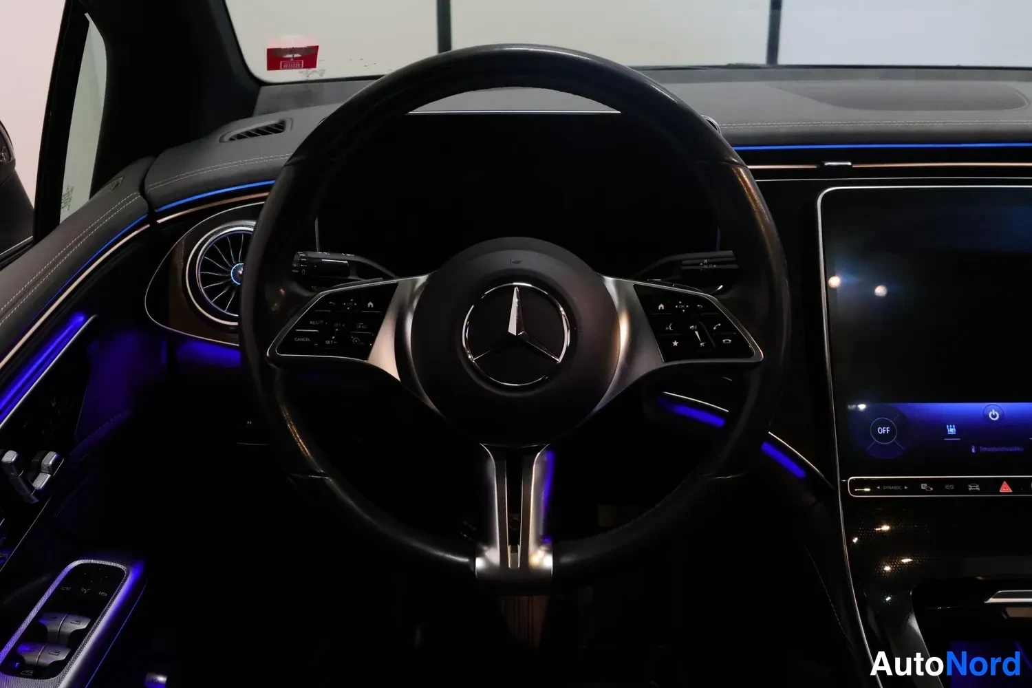 Muu: Mercedes-Benzin ohjaamon etunäkymä: multitoimintoratti, osittain pimeä mittaristonäyttö ja keskinäyttö, sininen ympäristövalaistus.