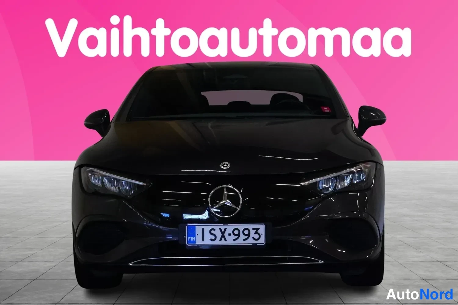 Edestä: Mercedes-Benz EQE -sedanin suora etukuva mustakilpiset etuvalot, Mercedes-tähti etusäleikössä ja rekisterikilpi näkyvät; auton ääriviivat heijastavat pinkin tau