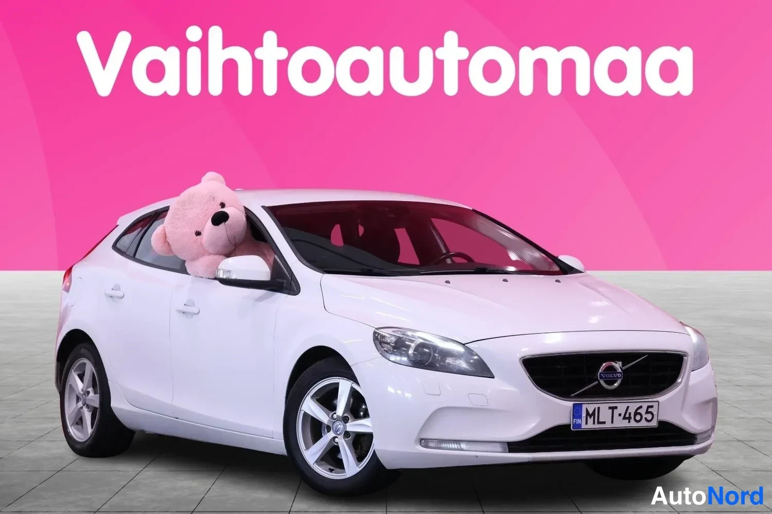 Etuviisto, nokka oikealle: Valkoinen Volvo V40 etuokolikuvassa, rekisteritunnus, pinkki tausta.