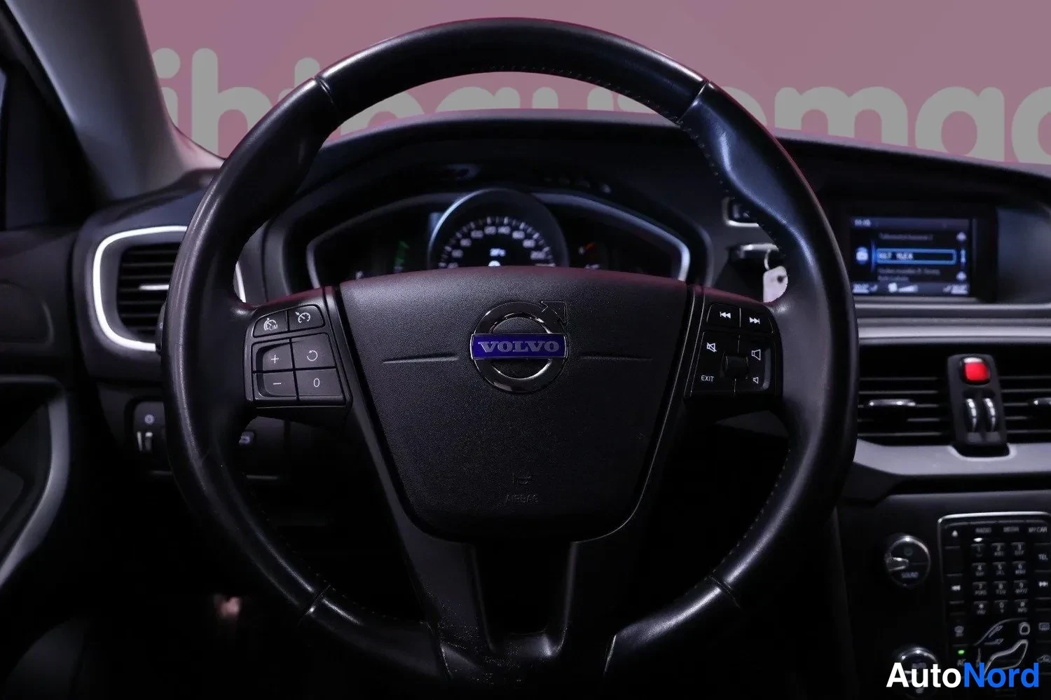 Muu: Volvo-ohjauspyörä ja kojelauta sisältä kuvattuna; mittaristo ja infotainment-näyttö näkyvät taustalla.