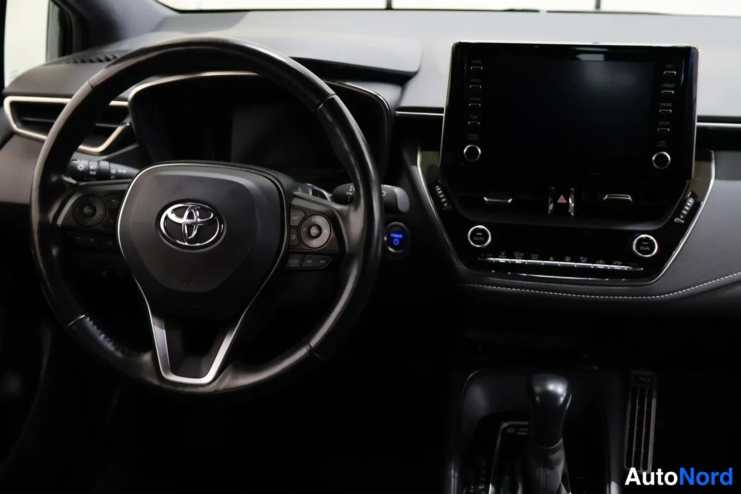Muu: Ohjaamon mitattu kuva: Toyota-merkki ohjauspyörässä, kosketusnäytöllinen infotainment-yksikkö ja automaattivaihteen valitsin.