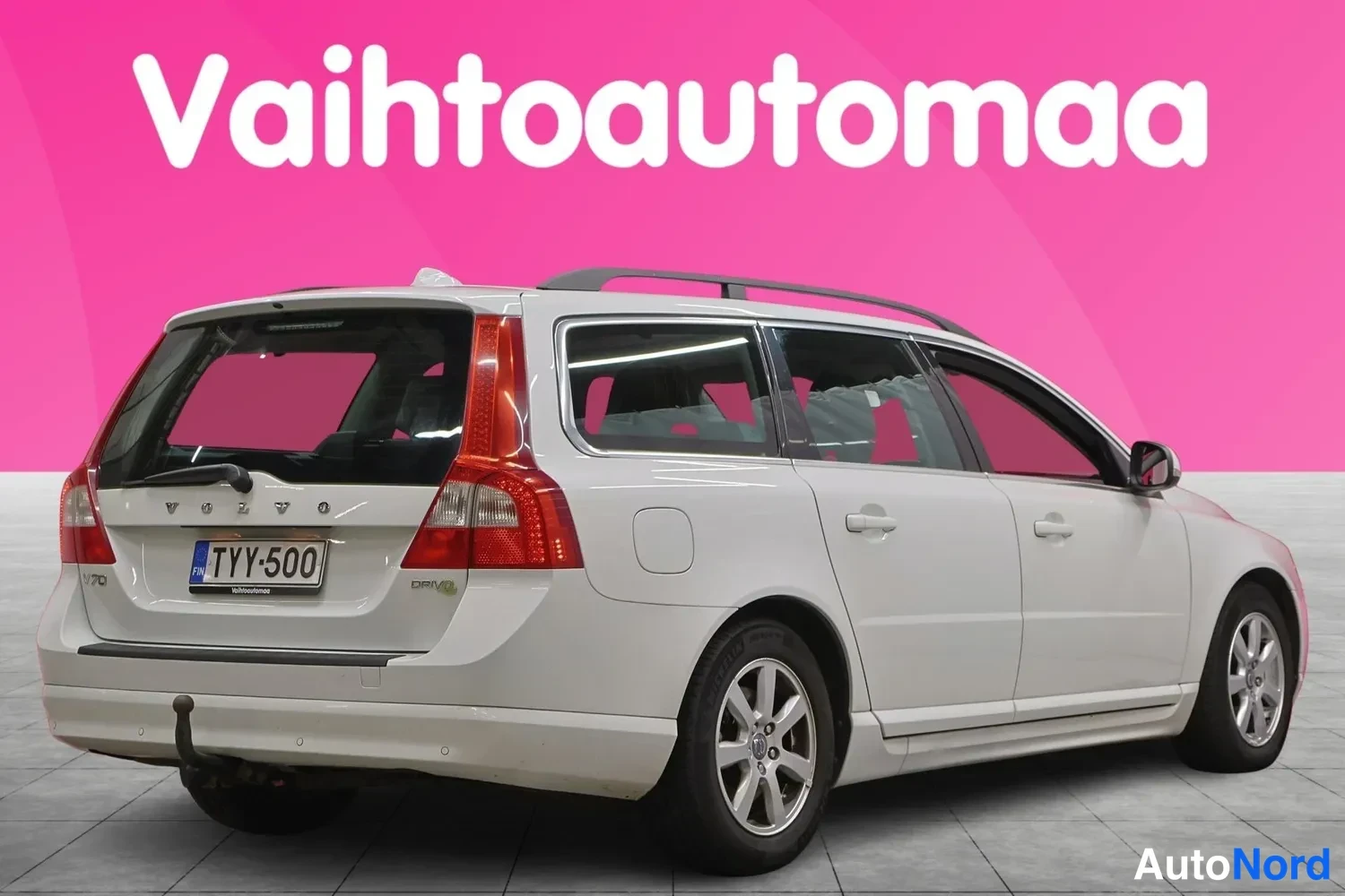 Takaviisto: Valkoinen farmariauto toiselta sivulta takaviistosta kuvattuna, takaosa ja rekisteri näkyvissä, pinkki tausta.