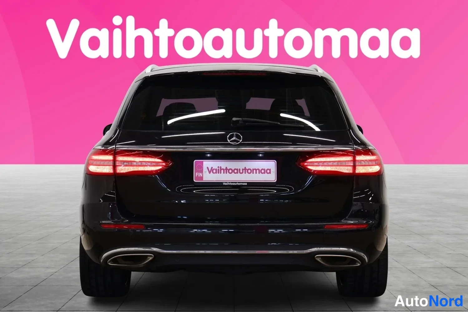 Takaa: Mustan Mercedes-Benz farmarin takaosa suoraan takaa; Mercedeksen tähti, LED-takavalot ja kaksi pakoputkea näkyvät vaaleanpunaista taustaa vasten.