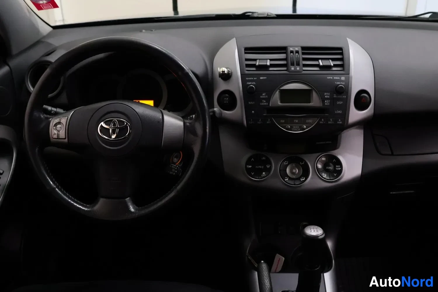 Muu: Ohjaamo kokonaisuudessaan: musta Toyota-ohjauspyörä, keskinäyttö ja radio ja erilliset pyöristys- ja lämpötilansäätimet, manuaalivaihteiston vaihdekeppi.