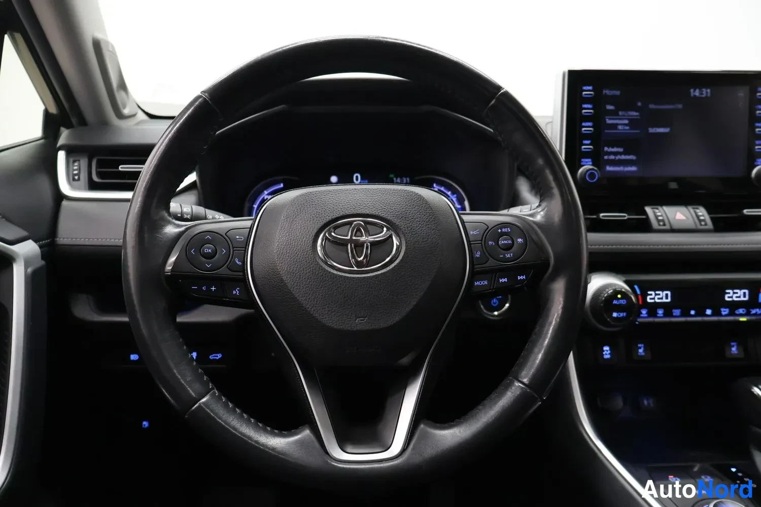 Muu: Ohjaamon näkymä Toyotasta: kuljettajan ohjauspyörä Toyota-logolla, kojelaudan näytöt ja keskikonsolin infotainment-näyttö.