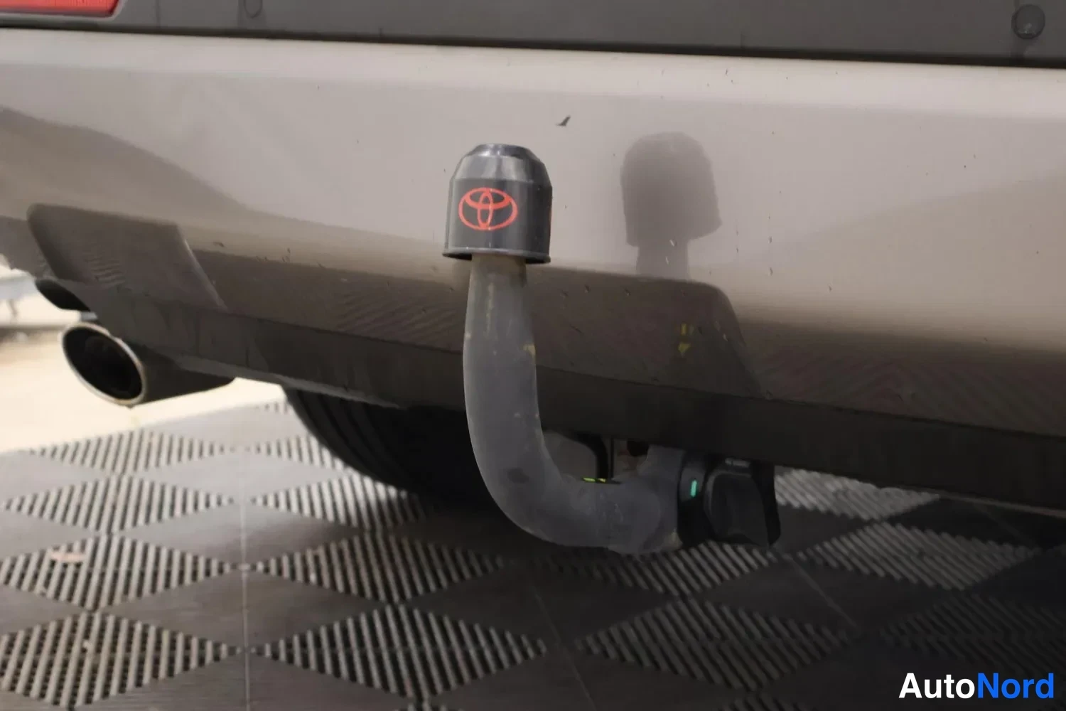 Yksityiskohta: Auton takaosassa näkyy jalusta, jossa on musta kansi ja punainen Toyota-logo, ja putki ulottuu maahan asti.