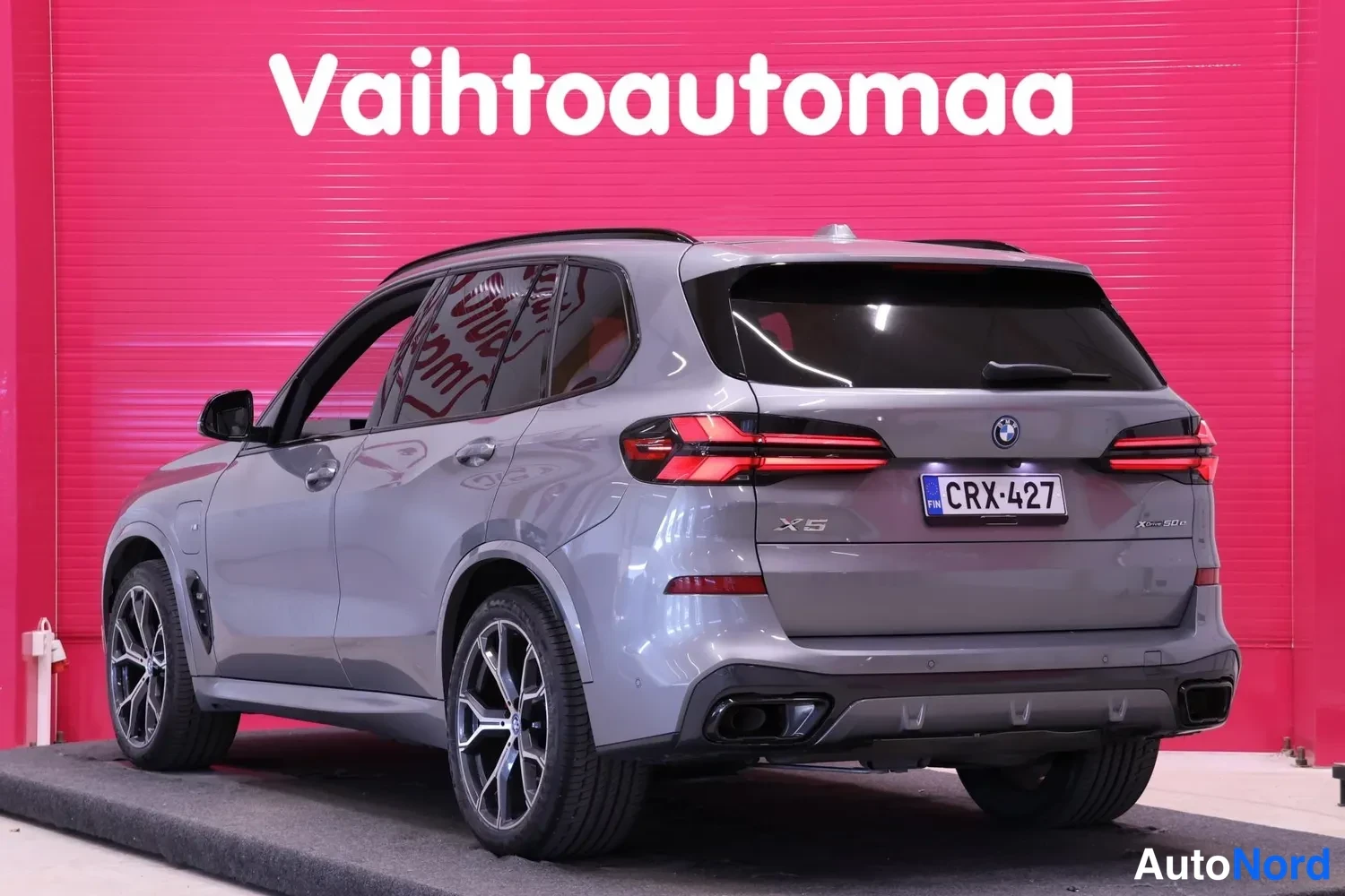 Takaviisto: Auton takakulmanäyttö: harmaa BMW X5 -tyyppinen katumaasturi takaa ja oikealta sivulta kuvattuna punaisella taustalla.