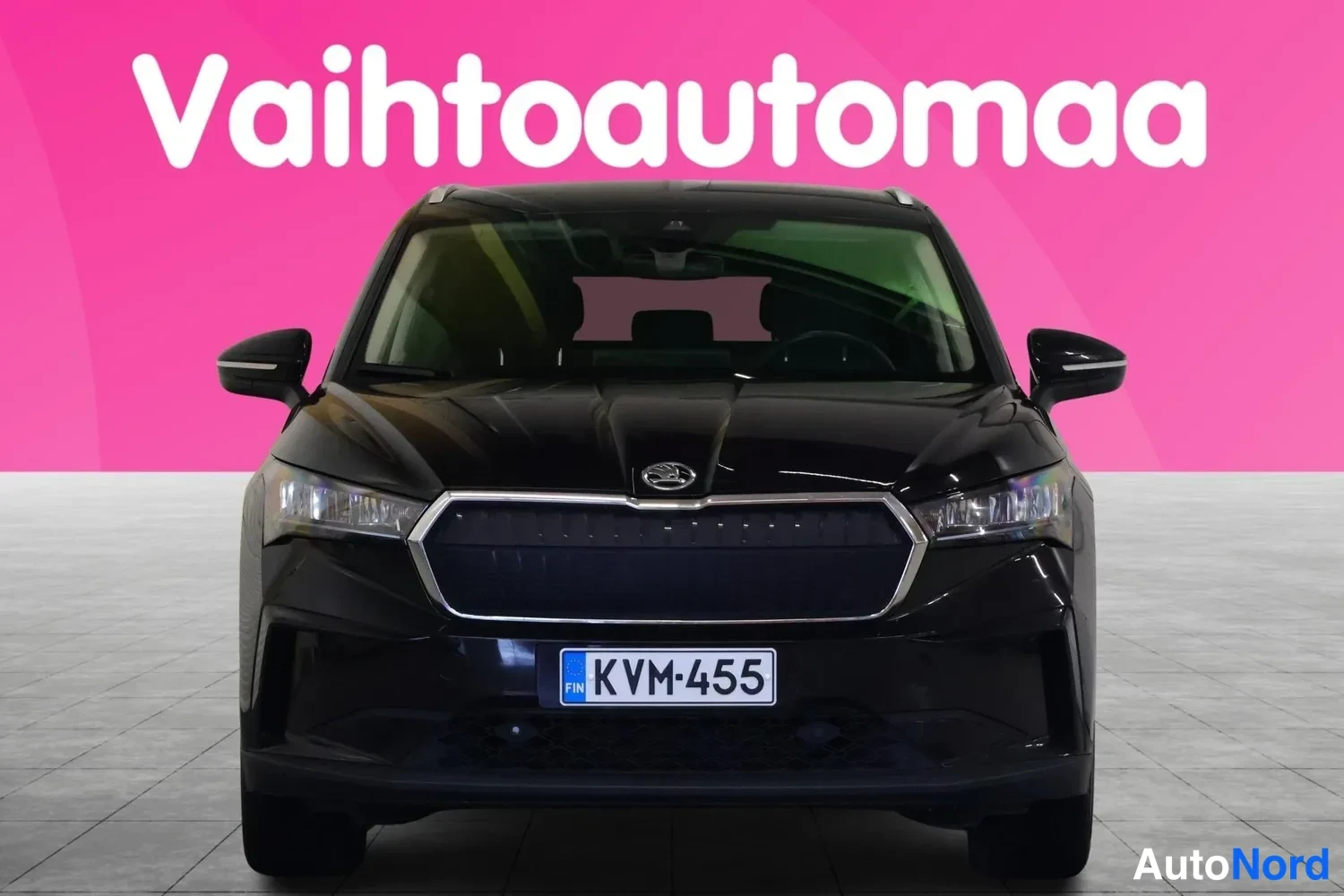 Edestä: Mustan automobiilin etunäku edestäpäin, rekisterikilpi, pinkki tausta tekstillä Vaihtoautomaa.