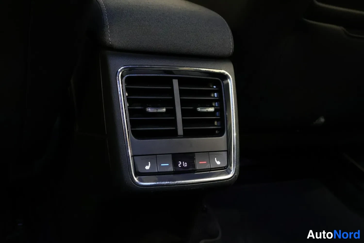 Yksityiskohta: Close-up view of rear interior HVAC control panel below headrest with digital display reading 21.0 and heated seat buttons on left and right
